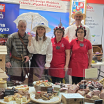 Przewodniczący wraz z przedstawicielami zwycięskiego Koła Gospodyń Wiejskich  Zakocie „Wygodni Zakociacy” pozujący do zdjęcia na stoisku na targach Grüne Woche w Belinie.